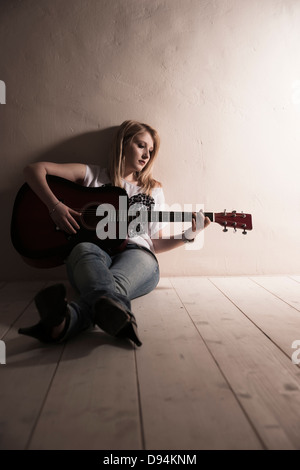Giovane donna seduta sul pavimento a suonare la chitarra in Studio Foto Stock