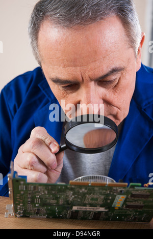 Uomo che guarda alla scheda a circuito stampato con lente di ingrandimento in Studio Foto Stock