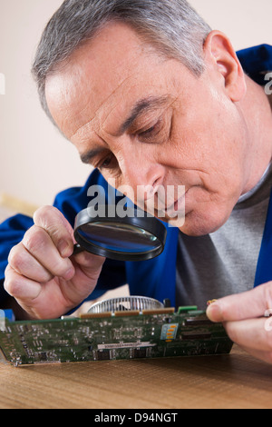 Uomo che guarda alla scheda a circuito stampato con lente di ingrandimento in Studio Foto Stock