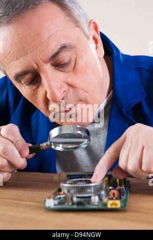 Uomo che guarda alla scheda a circuito stampato con lente di ingrandimento in Studio Foto Stock