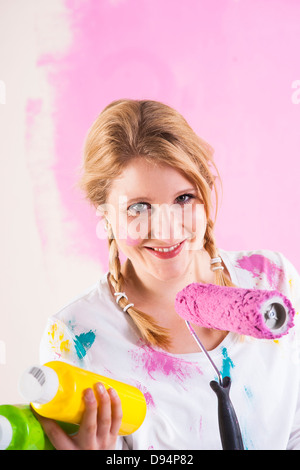 Studio shot della giovane donna che mantiene il rullo di vernice, di decidere tra i colori di vernice Foto Stock