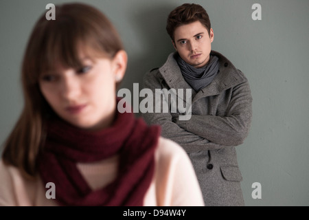 Ritratto di giovane uomo in piedi dietro il giovane donna, guardando il suo intensamente, Studio shot su sfondo grigio Foto Stock