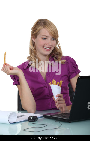 Donna di mangiare patatine fritte alla sua scrivania Foto Stock