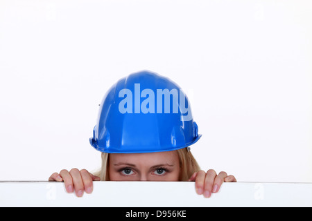 Tradeswoman di sbirciare da dietro un muro basso Foto Stock