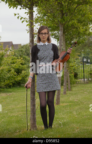 I vecchi ragazza adolescente tenendo un violino in piedi in un prato con alberi. Foto Stock