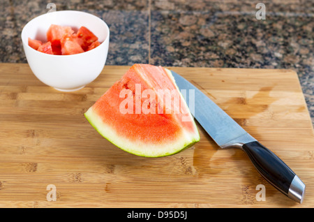 Anguria a fette con il coltello di taglio, ciotola e tavola di legno Foto Stock