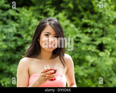 Foto orizzontale della giovane donna adulta guardando in avanti tenendo bere fuori con sfocato verdi alberi in background Foto Stock