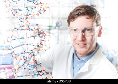 Germania, Ritratto di giovane scienziato con modello di DNA, sorridente Foto Stock