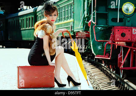 Retrò ragazza seduta sulla valigia presso la stazione ferroviaria Foto Stock