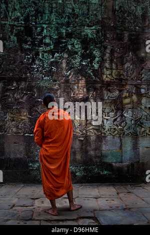 Monaco buddista guardando bassorilievi sulla parete esterna del condotto esterno del tempio Bayon, Angkor, Cambogia Foto Stock