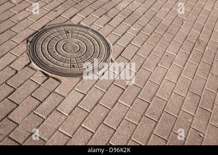 In tondo di acciaio tombino fognario sul cobblestone pavement Foto Stock