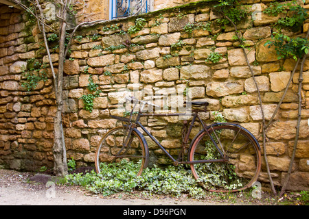 Rusty bicicletta appoggiata contro il vecchio muro di pietra con ivy a Sarlat, Dordogne regione della Francia Foto Stock