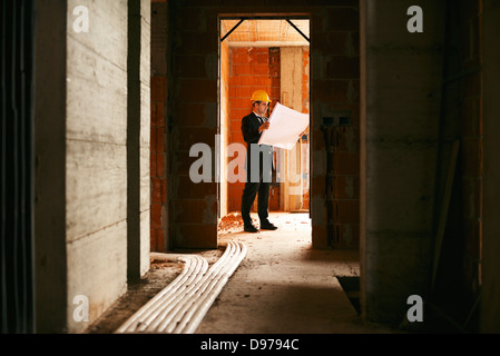 Ingegnere al lavoro in cantiere, in piedi in appartamento edificio e guardando il blueprint e piani Foto Stock