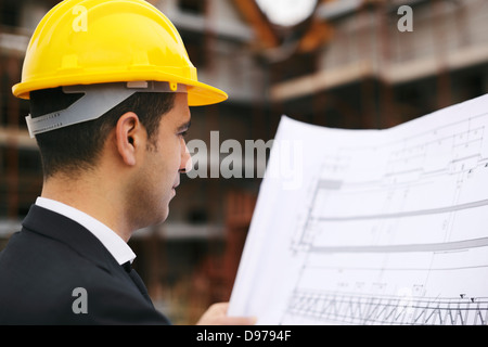 Giovane uomo che lavora come ingegnere in nuovi edifici di appartamenti, guardando il piano di costruzione nel sito in costruzione Foto Stock