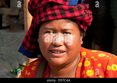 Donna che indossa rosso luminoso controllato copricapo sorridente in telecamera in un mercato in Myanmar (Birmania) Foto Stock