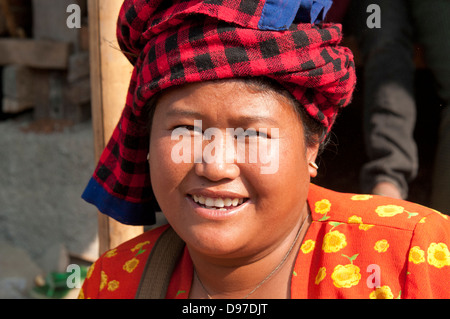 Donna che indossa rosso luminoso controllato copricapo sorridente in telecamera in un mercato in Myanmar (Birmania) Foto Stock