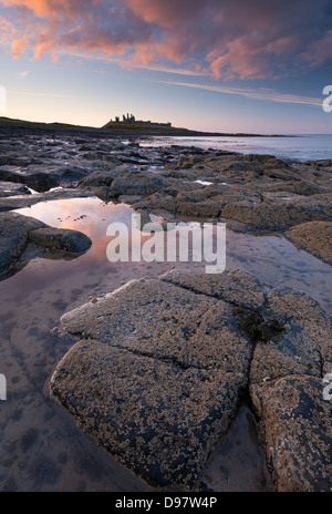 Il tramonto sopra il castello di Dunstanburgh, Northumberland, Inghilterra. Molla (maggio) 2013. Foto Stock