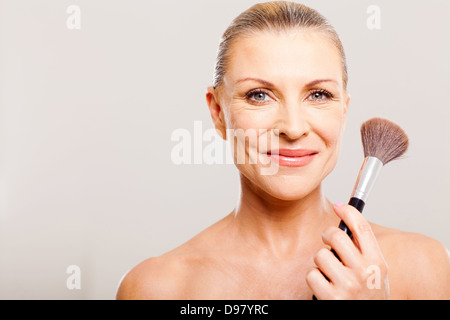 Bella donna senior dopo applicazione di make up tenendo un pennello Foto Stock