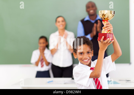 Felice maschio scuola elementare studente tenendo un trofeo in aula Foto Stock