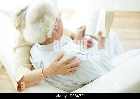 Grigio-dai capelli uomo anziano e sua moglie libro di lettura a casa Foto Stock
