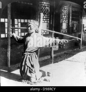 La giustizia cinese: prigioniera, inginocchiata sulle catene alle caviglie in una forma di scorte, bracci oustretched supportato da pollici legati dalla corda ad un palo. Uno di una coppia di immagini da una scheda stereografica c1906. Materia penale Foto Stock