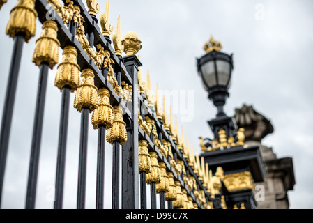 Porte dorate del Palazzo Reale di Bruxelles Bruxelles Belgio | BRUXELLES, Belgio — Nappe dorate adornano i cancelli perimetrali in ferro nero del Palazzo Reale di Bruxelles, incorniciando una vista verso un lampione sormontato da una corona al pilastro del cancello. Le decorazioni in ferro risalgono alla vasta ricostruzione del palazzo voluta da Re Leopoldo II, completata a tappe all'inizio del XX secolo. Il palazzo funge da sede amministrativa del sovrano piuttosto che da residenza; la famiglia reale vive al Castello di Laeken. Foto Stock