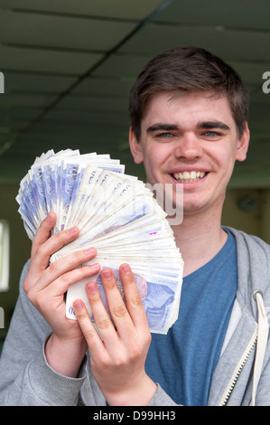 Felice giovane tenendo un fan di venti pound note per un totale di tre mila libbre Foto Stock