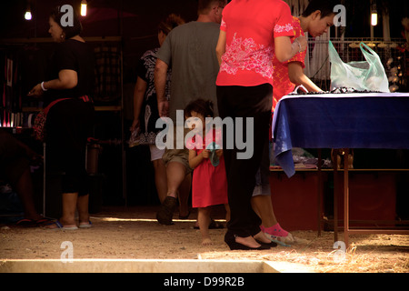 WAT MERCATO KARON, KARON, Phuket, Tailandia 9 FEBBRAIO 2013: un bambino funziona si erge con la sua mamma al loro mercato in stallo in Thailandia Foto Stock