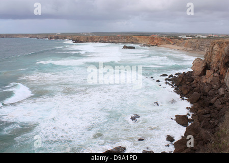 Robusto e scogliere della costa Algarve in Sagres Portogallo, sull'Oceano Atlantico sotto il buio cielo di pioggia Foto Stock