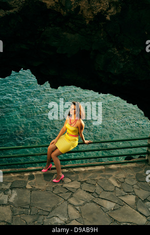 Pretty girl in abito giallo seduti sul recinto affacciato sul mare Foto Stock