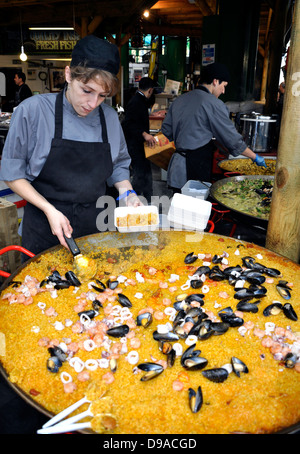 Lo Chef femmina cucinare e servire la paella Street Food al Mercato di Borough, Londra Foto Stock