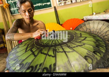 Giugno 14, 2013 - Pathein, Ayeyarwady, Unione di Myanmar - un lavoratore vernici ombrelli impermeabile a Shwe Sar fabbrica ombrello di Pathein. Pathein è un centro della giunta birmana ombrellone e ombrellone industria. La maggior parte sono effettivamente ombrelloni realizzati nel tradizionale modo birmano utilizzando carta trattata che non è a prova d'acqua. Shwe Sar ombrelloni sono realizzati con stoffa trattata e sono impermeabili. Poiché noi e le sanzioni europee sono state abolite le aziende in Myanmar hanno visto un'esplosione delle esportazioni. Shwe Sar esporta la maggior parte di loro ombrelli per l'Europa. Pathein, a volte chiamato anche Bassein, è una città portuale un Foto Stock