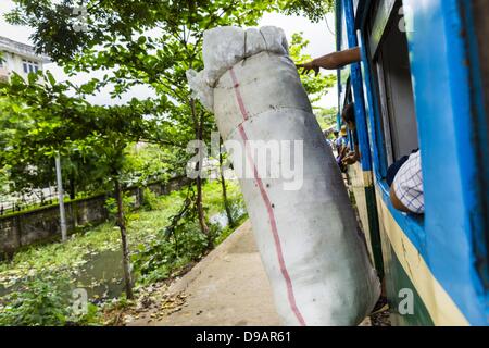 Yangon, Unione di Myanmar. Il 15 giugno, 2013. Un passeggero che genera un fascio di bottiglie di plastica era il riciclaggio off il treno come lo tira dentro il suo arresto. L Arcidiocesi di Yangon ferroviaria circolare è il locale dei pendolari rete ferroviaria che serve il Yangon area metropolitana. Azionato da Myanmar Ferrovie, 45,9-chilometro (28.5Â mi) 39-stazione di sistema ad anello collega città satelliti e zone di periferia della città. La ferrovia ha circa 200 autobus, esegue 20 volte e vende 100.000 a 150.000 biglietti giornalieri. Il loop che richiede circa tre ore per completare, è un popolare per i turisti a vedere una sezione della vita in Y Foto Stock