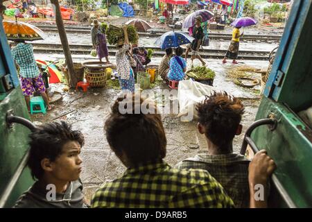 Yangon, Unione di Myanmar. Il 15 giugno, 2013. Ragazzi sedersi nella porta di Yangon treno circolare come si tira in una stazione. L Arcidiocesi di Yangon ferroviaria circolare è il locale dei pendolari rete ferroviaria che serve il Yangon area metropolitana. Azionato da Myanmar Ferrovie, 45,9-chilometro (28.5Â mi) 39-stazione di sistema ad anello collega città satelliti e zone di periferia della città. La ferrovia ha circa 200 autobus, esegue 20 volte e vende 100.000 a 150.000 biglietti giornalieri. Il loop che richiede circa tre ore per completare, è un popolare per i turisti a vedere una sezione della vita di Yangon. I treni da 3:45 Foto Stock