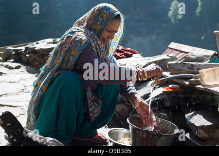 Un Gaddi tribali lavaggi la matriarca della famiglia piatti presso il villaggio himalayana di Kugti in Himachal Pradesh, India Foto Stock