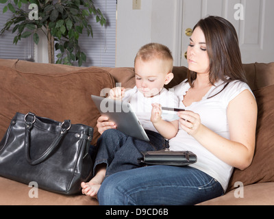 Giovane donna caucasica si siede con toddler maschio sul suo giro sul lettino in casa nel salotto acquisti online tramite carta di credito. Foto Stock
