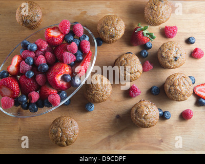 Frutta muffin appena sfornato collocato su un tavolo di legno a fianco di fragole, lamponi e mirtilli. Foto Stock