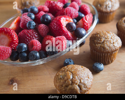 Frutta muffin appena sfornato collocato su un tavolo di legno a fianco di fragole, lamponi e mirtilli. Foto Stock