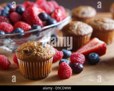 Frutta muffin appena sfornato collocato su un tavolo di legno a fianco di fragole, lamponi e mirtilli. Foto Stock