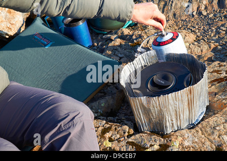 Un escursionista cucinare su un fornello da campeggio sulla cima di una montagna nel distretto del lago. Foto Stock