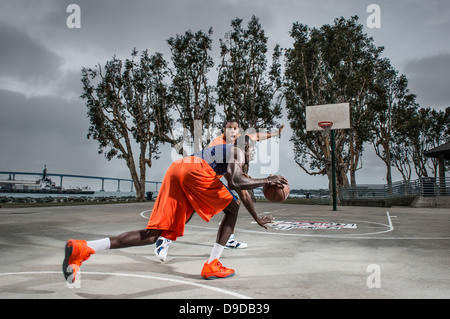 Giovani uomini giocare a basket su corte Foto Stock