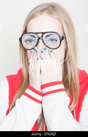 Ragazza indossando occhiali finti con le mani che coprono la bocca Foto Stock