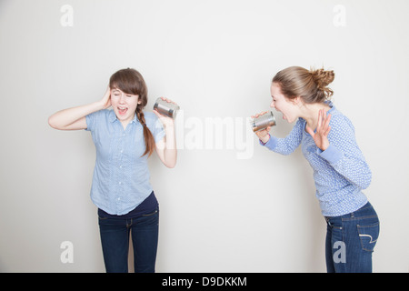 Due ragazze con le lattine di lattina, uno grida e uno riguardante il suo orecchio Foto Stock