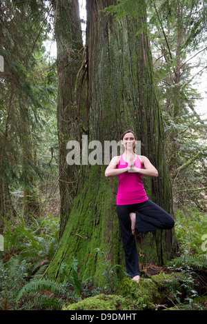 Donna matura eseguendo la posizione dell'albero nella foresta Foto Stock