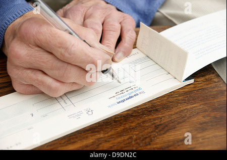 Donna anziana la scrittura di un controllo che è sempre più raro in questi giorni (Co-operative bank check book) Co operativa facce banca nazionalizzazione) Foto Stock