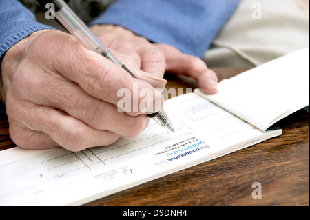 Donna anziana la scrittura di un controllo che è sempre più raro in questi giorni (Co-operative bank check book) Co operativa facce banca nazionalizzazione) Foto Stock