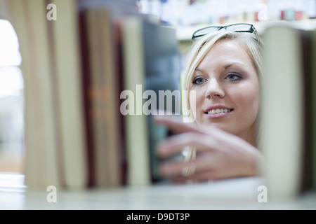 Studentessa scegliendo libro in biblioteca Foto Stock