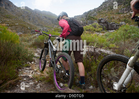 Giovane donna spingendo mountain bike su percorso di montagna Foto Stock