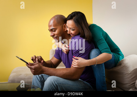 Metà adulto giovane seduto sul divano guardando a tavoletta digitale Foto Stock