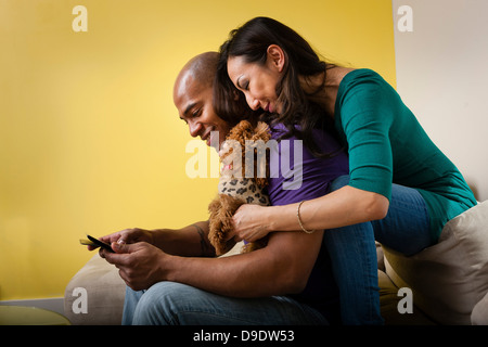 Metà adulto giovane seduto sul divano con il cane e lo smartphone Foto Stock